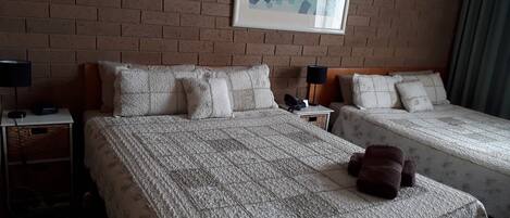 Habitación de hotel con dos camas, un muro de ladrillo, una obra de arte enmarcada y un osito de peluche sobre la cama.