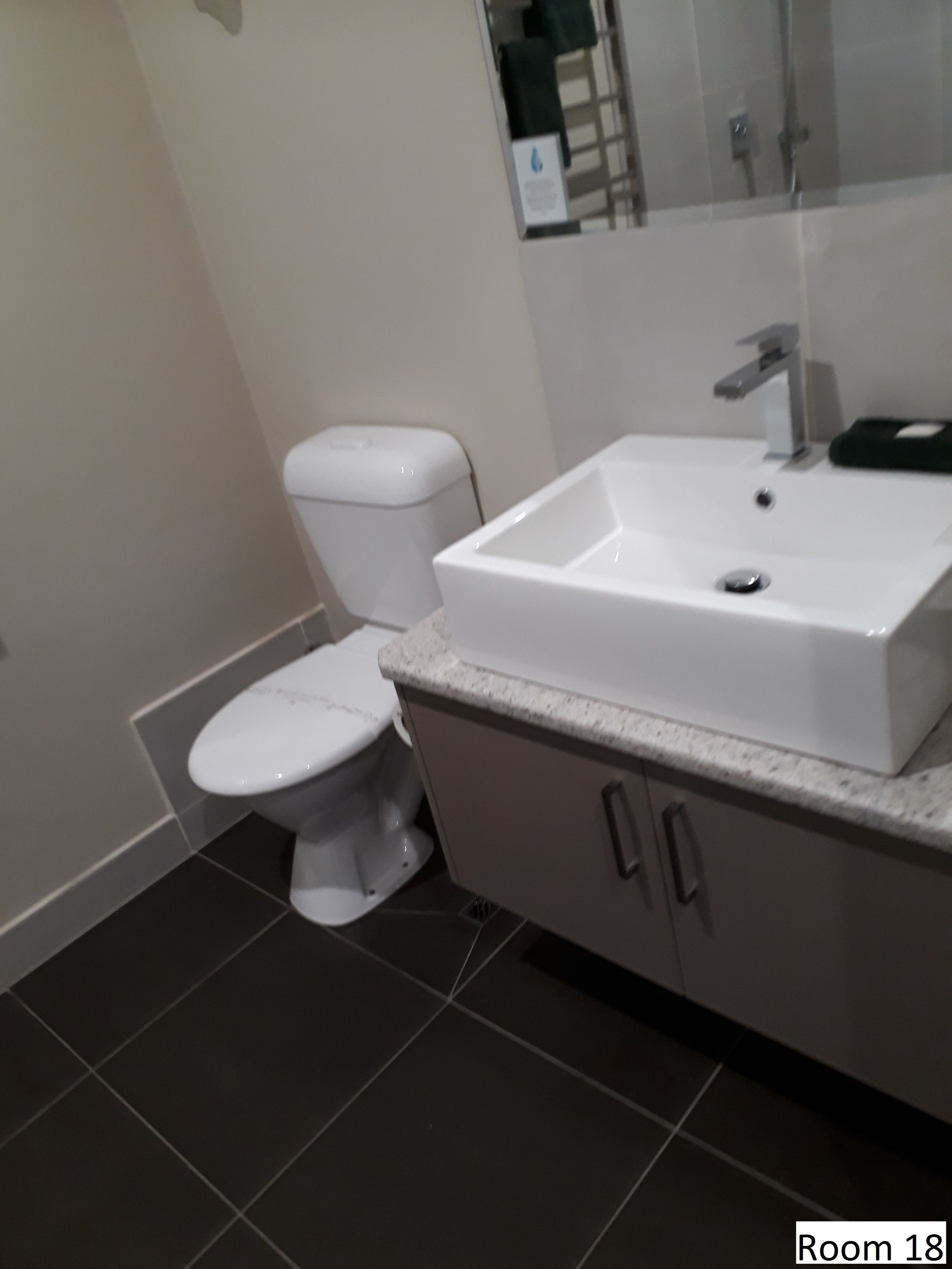 A bathroom with a white toilet, a white sink, and a mirror above the sink. The floor is tiled.