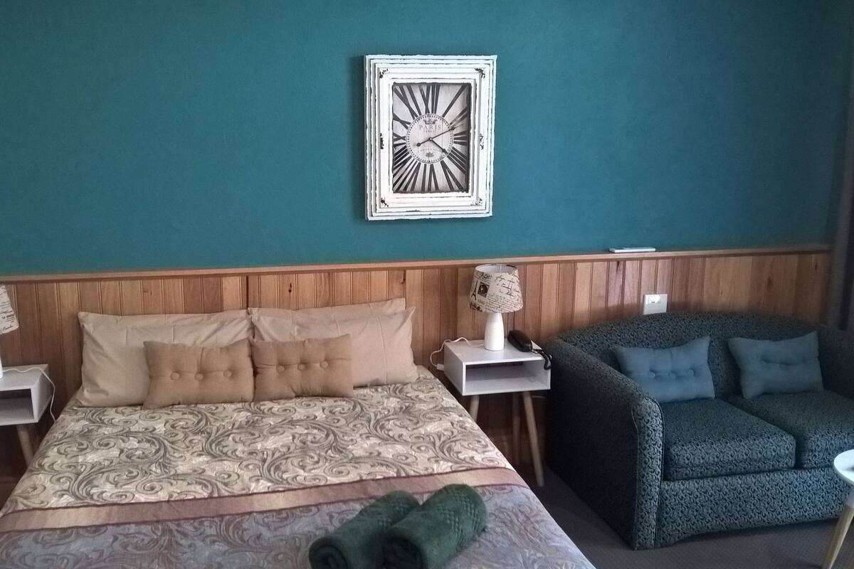 Ett hotellrum med en säng, en soffa, en väggklocka och ett litet bord.