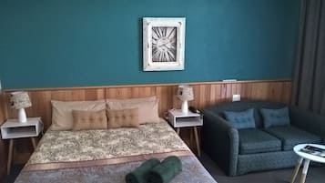 A hotel room with a bed, a sofa, a wall clock, and a small table.