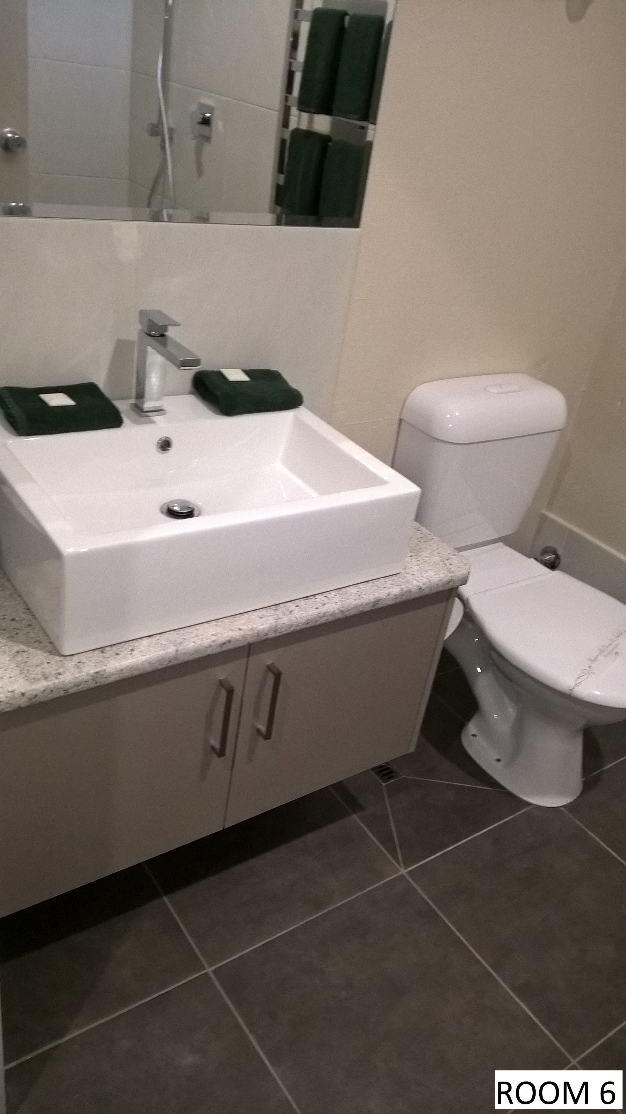 Un baño con un lavabo blanco, un inodoro y un espejo sobre el lavabo. Dos toallas cuelgan de un perchero.