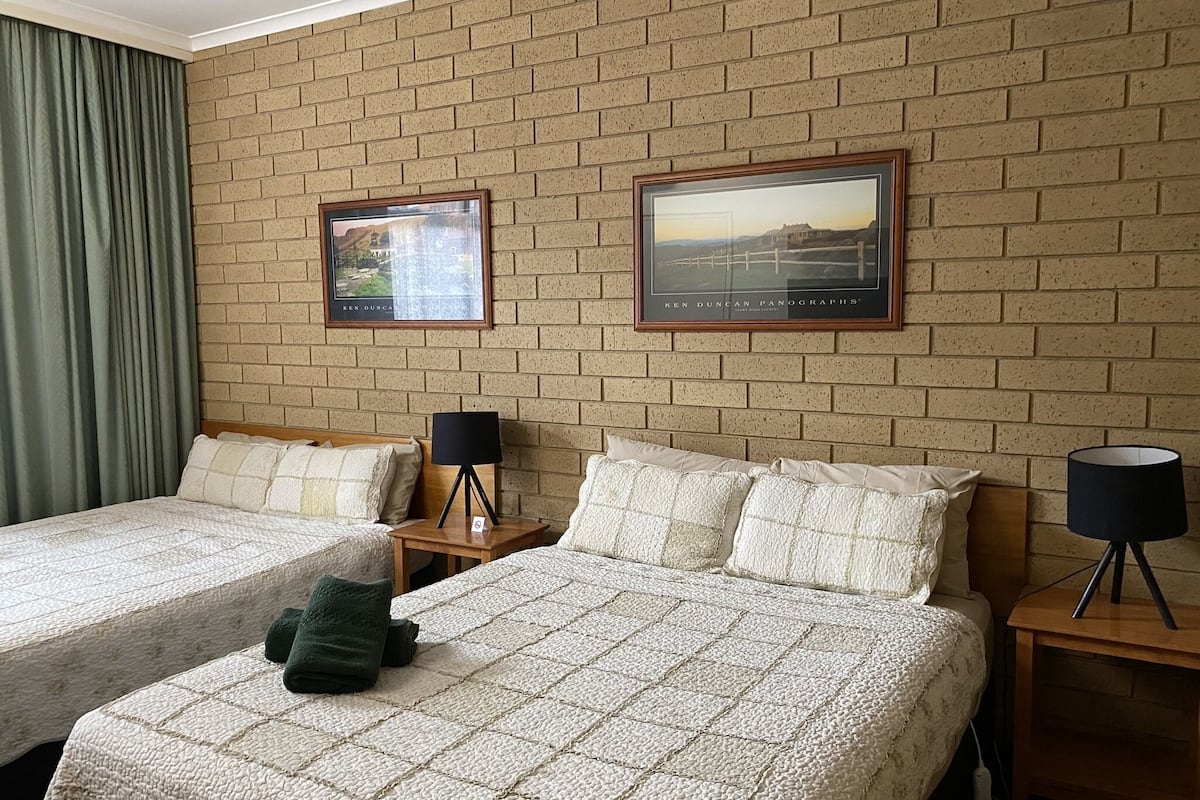 Ett hotellrum med två sängar, en tegelvägg och två inramade tavlor.