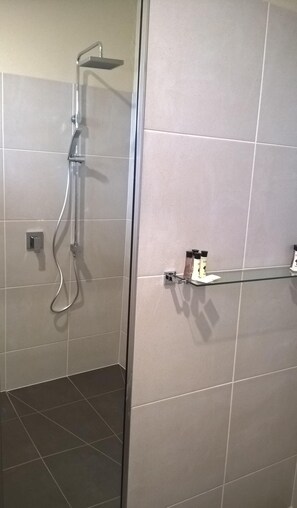 A shower area with a glass door, a showerhead, and a small shelf with toiletries.
