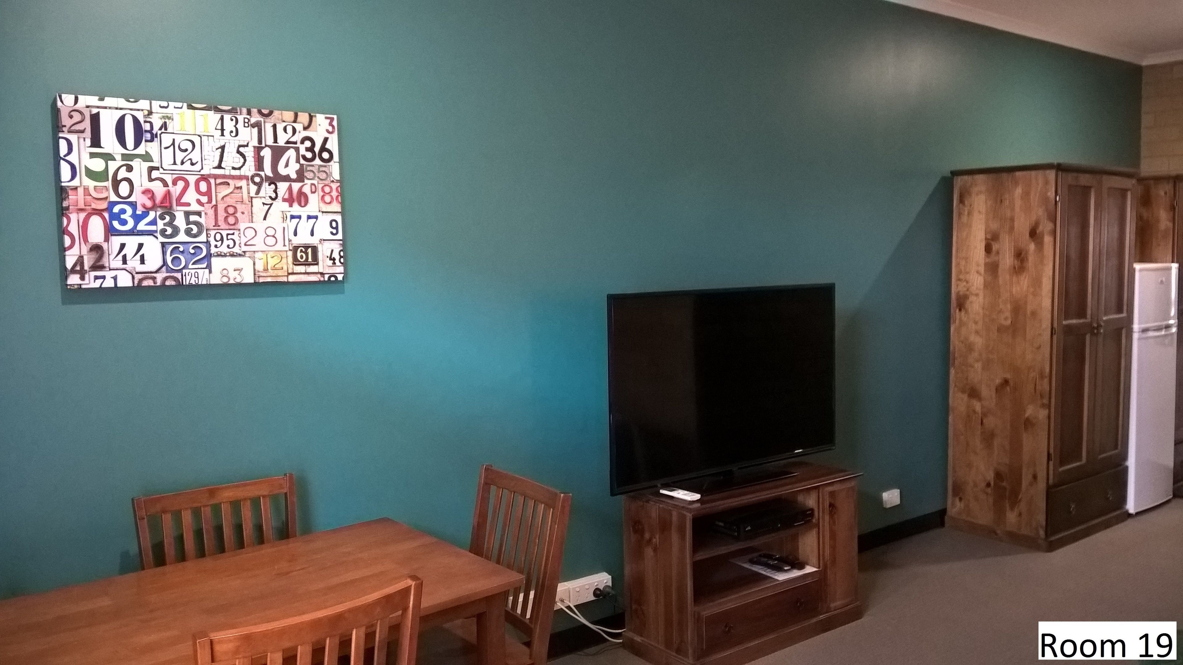 A room with teal walls, a wooden table with chairs, a television on a wooden stand, and a wooden cabinet.