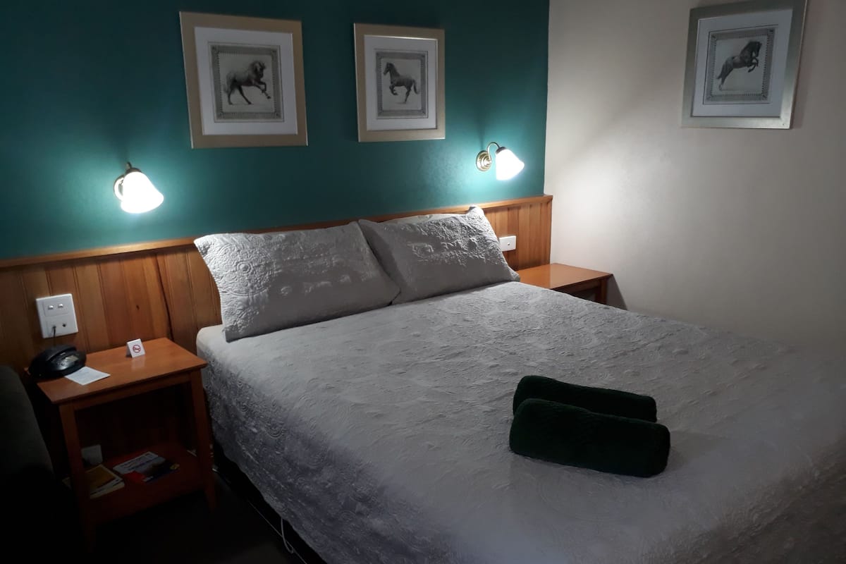 Ett hotellrum med en säng, två sängbord, en telefon, en skylt och inramade tavlor på väggen.