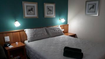 A hotel room with a bed, two bedside tables, a telephone, a sign, and framed pictures on the wall.