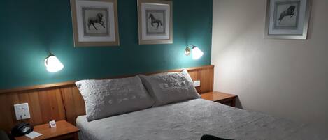 A hotel room with a bed, two bedside tables, a telephone, a sign, and framed pictures on the wall.