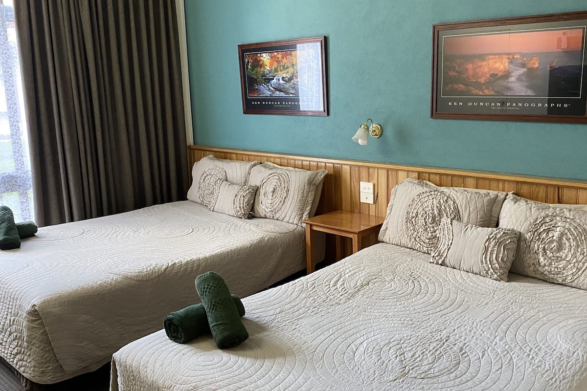 Ett hotellrum med två sängar, ett nattduksbord och två inramade panoramabilder på väggen.