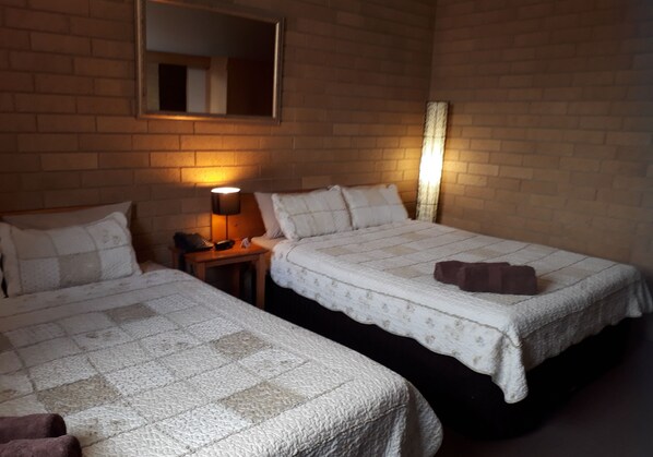 A hotel room with two beds, a mirror, a lamp, and a brick wall.