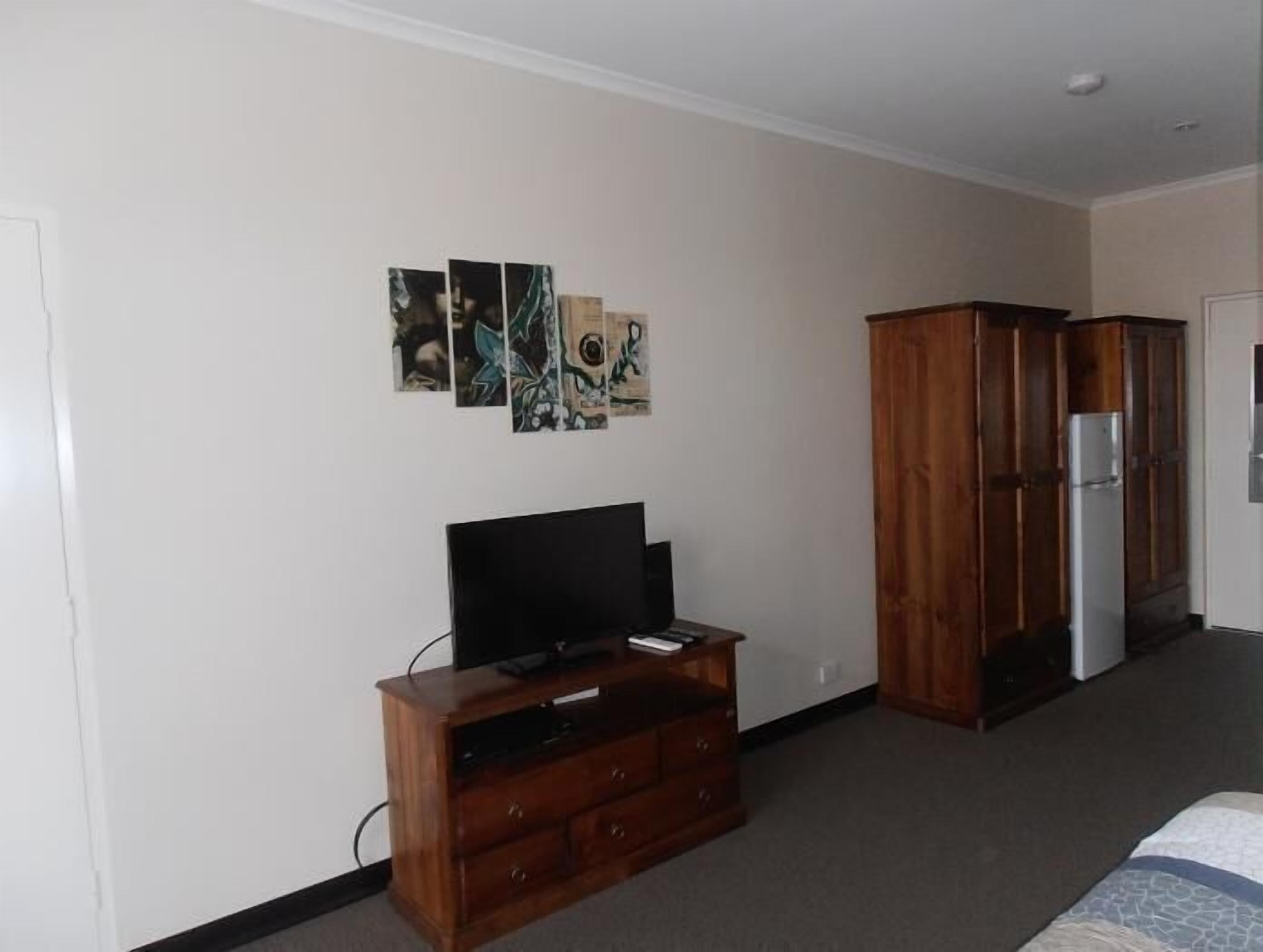 A bedroom with a wooden dresser, a flat-screen TV, and a refrigerator.