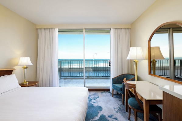 A hotel room with a bed, a desk, a chair, a large mirror, and a balcony with a view of the ocean. - NOAH'S On The Beach (Newcastle East)