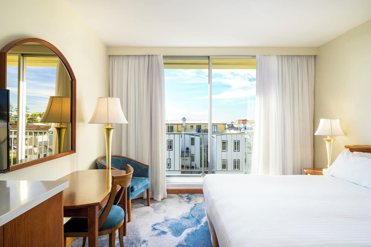 A hotel room with a bed, a desk, a chair, a TV, and a large window with curtains.