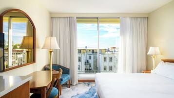 A hotel room with a bed, a desk, a chair, a TV, and a large window with curtains.