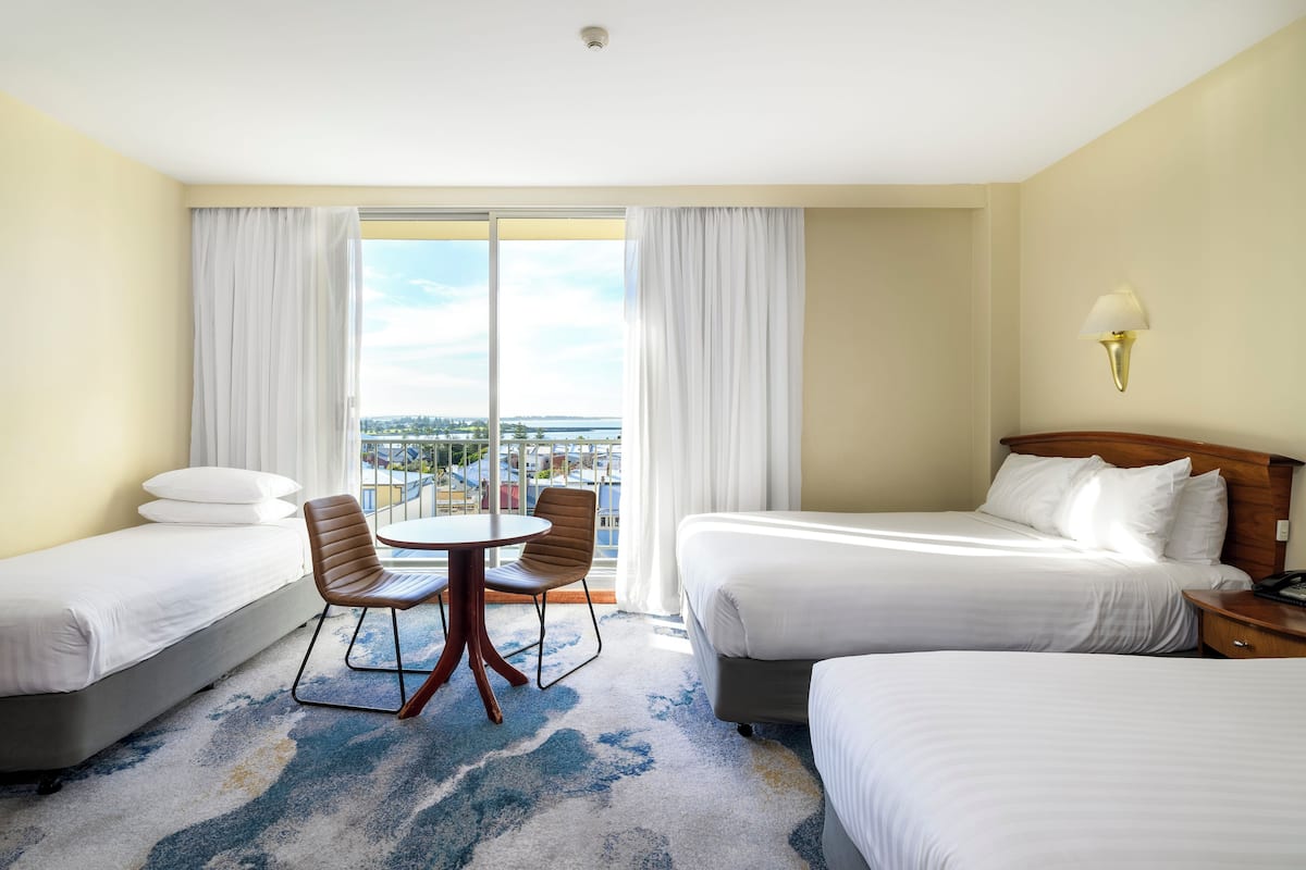 A hotel room with two beds, a dining table with chairs, and a view of the city.