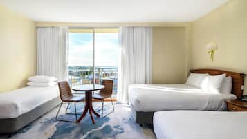 A hotel room with two beds, a dining table with chairs, and a view of the city.