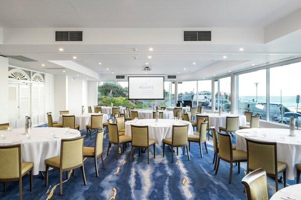 Une salle de conférence équipée de tables rondes, de chaises et d’un grand écran affichant le texte « NOAH’S NEWCASTLE ».