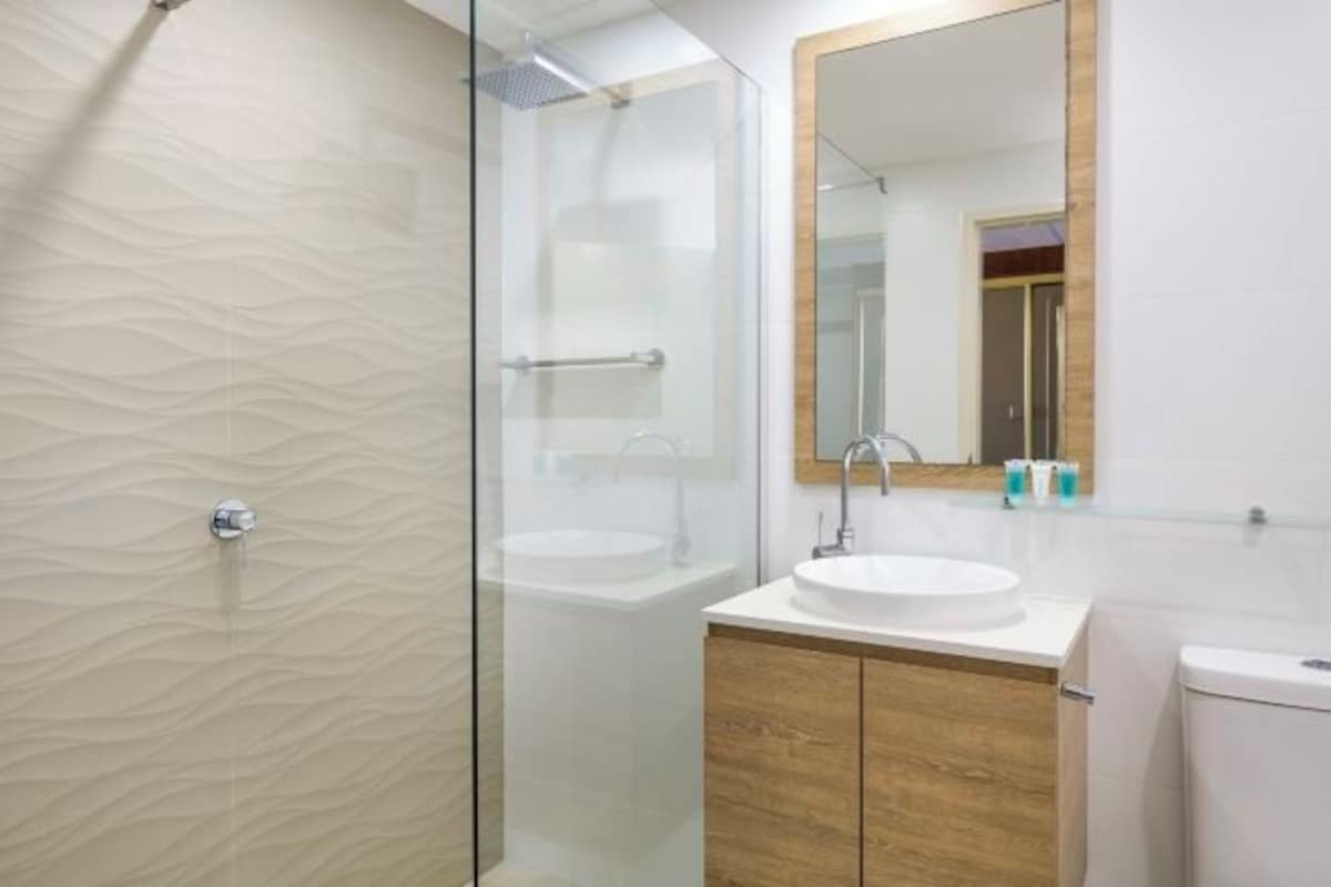 A modern bathroom with a glass-enclosed shower, a white sink, and wooden cabinets.