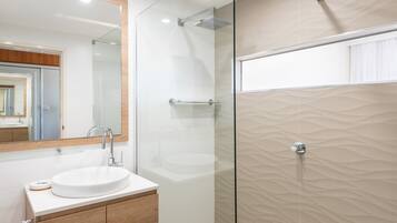 A modern bathroom with a glass-enclosed shower, a round sink, and a large mirror.