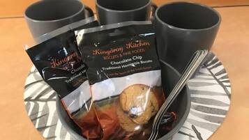 A tray with three black mugs and a bowl containing a packet of chocolate chip biscuits and a spoon.