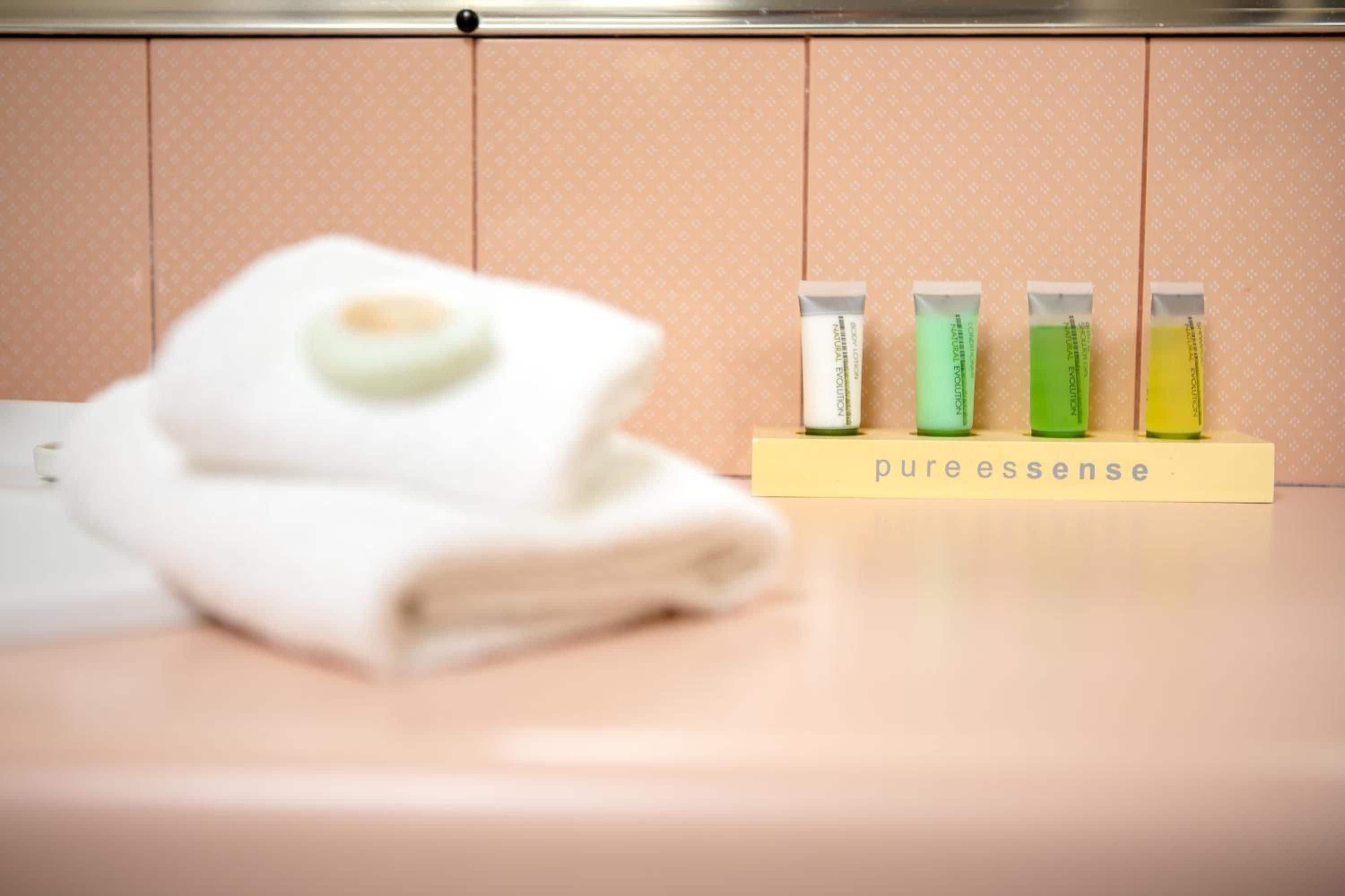 A bathroom with a towel and four bottles of PureEssence on a yellow stand.