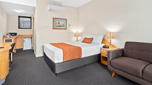 A hotel room with a bed, desk, chair, and a small kitchenette.