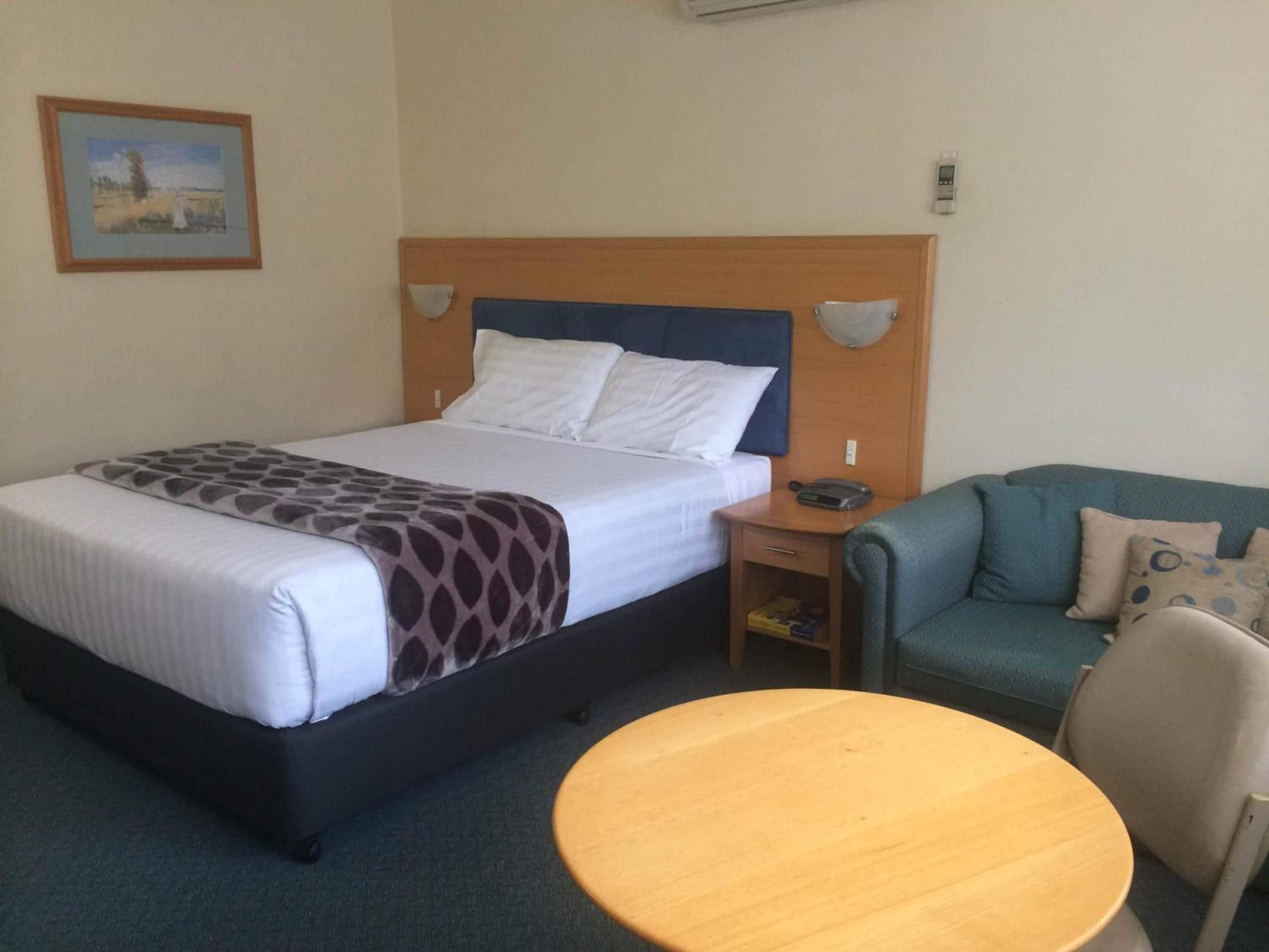 A hotel room with a bed, a bedside table with a phone, a small table, and a couch.