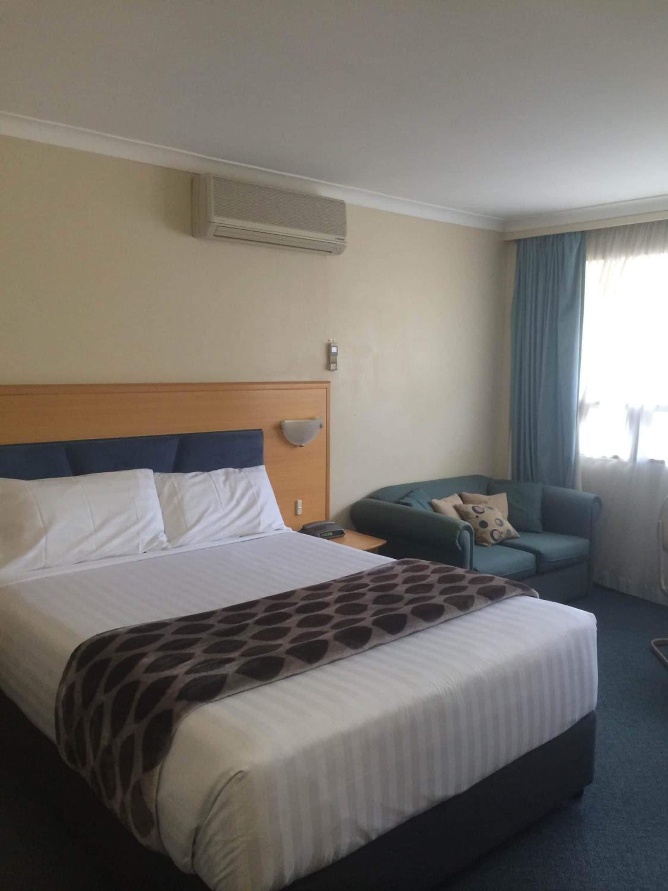 Ett hotellrum med en stor säng, ett nattduksbord, en stol och ett fönster med gardiner.