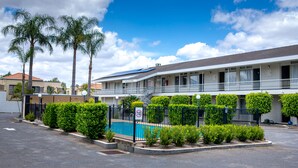 A hotel with a swimming pool, palm trees, and a clear blue sky. - Park Motor Inn (East Toowoomba)