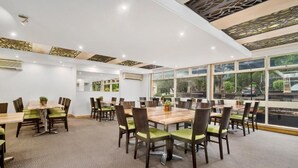 A spacious conference room with multiple tables and chairs, large windows offering a view of the outdoors, and a modern ceiling design.