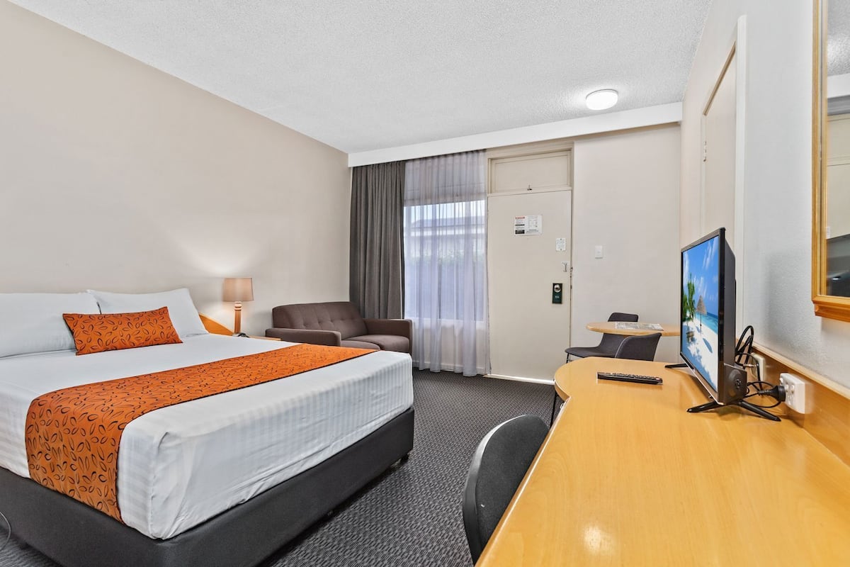 Quarto de hotel com cama, escrivaninha, cadeira, televisão e porta.