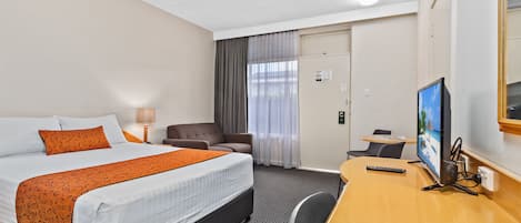 A hotel room with a bed, a desk, a chair, a TV, and a door.