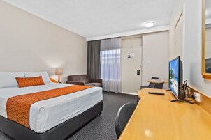Habitación de hotel con cama, escritorio, silla, televisor y puerta.