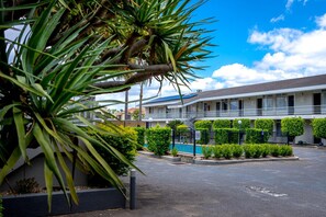 A hotel with a swimming pool, a fenced parking area, and a building with a balcony.