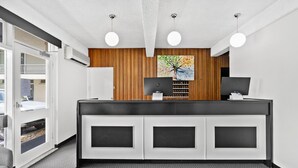 A reception area with a wooden panel wall, two computer monitors, a white reception desk, and a gray carpeted floor. - Park Motor Inn (East Toowoomba)
