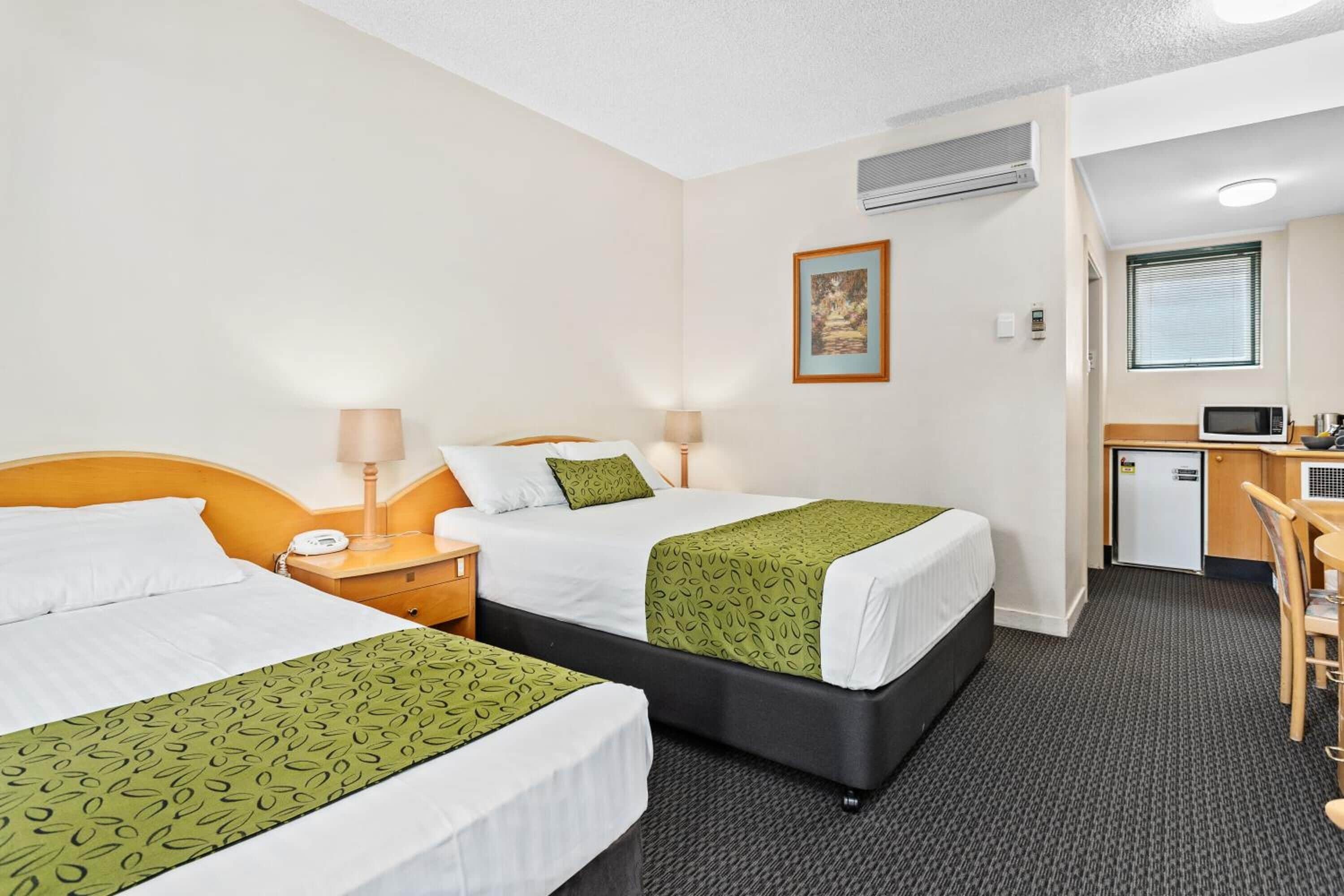 A hotel room with two beds, a desk, a microwave, and an air conditioning unit.