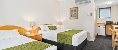 A hotel room with two beds, a desk, a microwave, and an air conditioning unit.