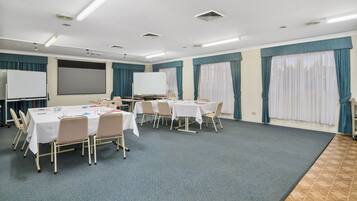 A conference room with tables, chairs, a whiteboard, and a projector screen.