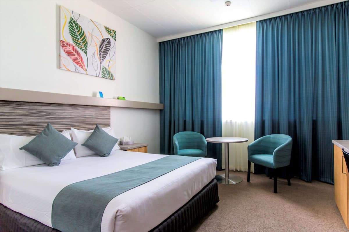 Hotellihuone, jossa on suuri sänky, kaksi tuolia, pieni pöytä ja taulu seinällä.