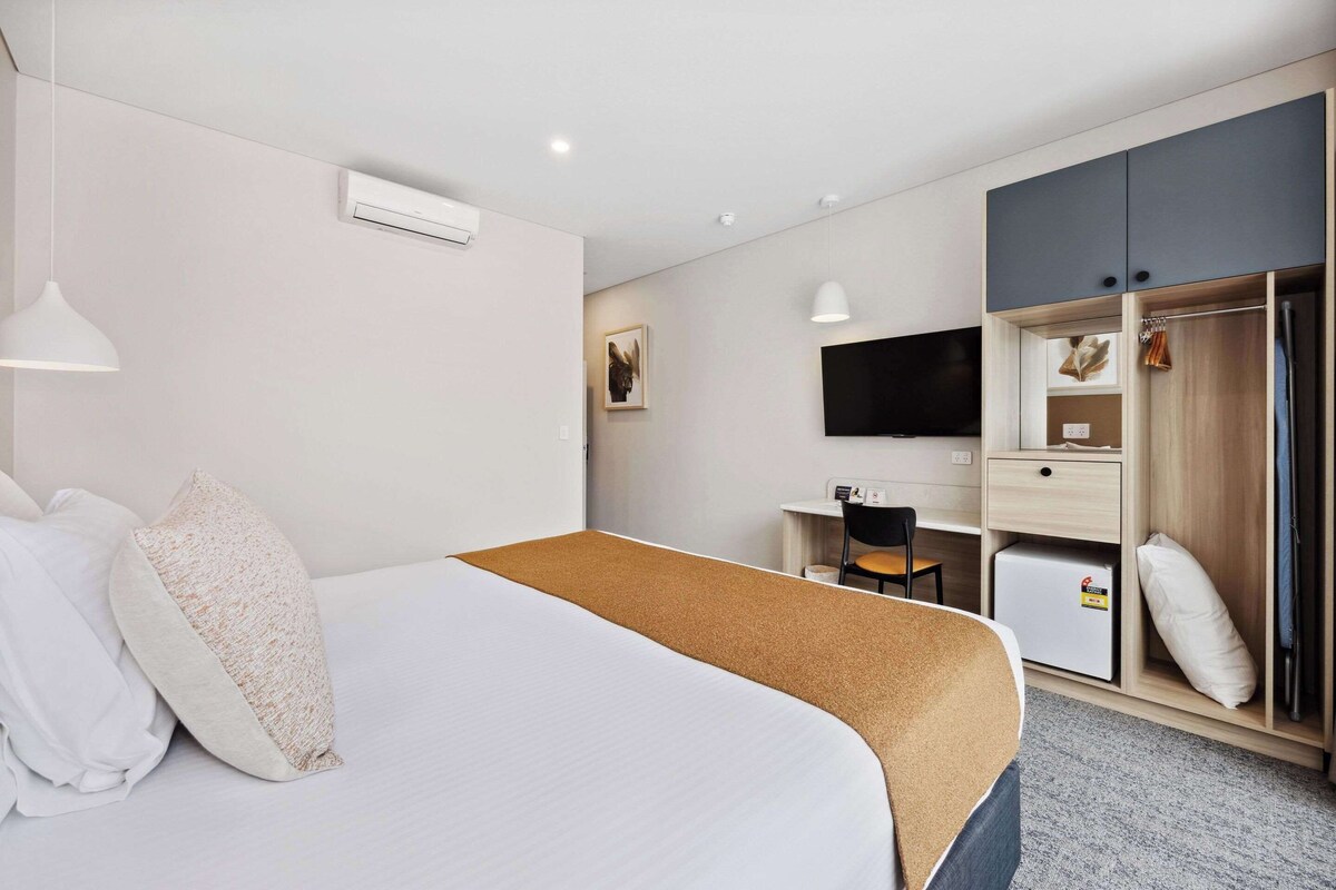 Una habitació d'hotel amb un llit gran, una taula, una cadira, un televisor i un armari.