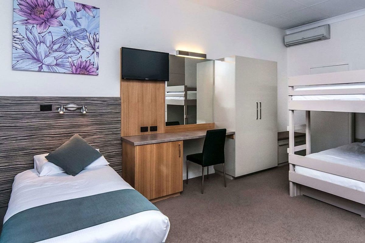 Hotellihuone, jossa on sänky, työpöytä, tuoli ja kerrossänky.