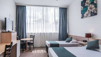 Habitación de hotel con dos camas, un escritorio, una silla, un televisor y un ventilador de techo.