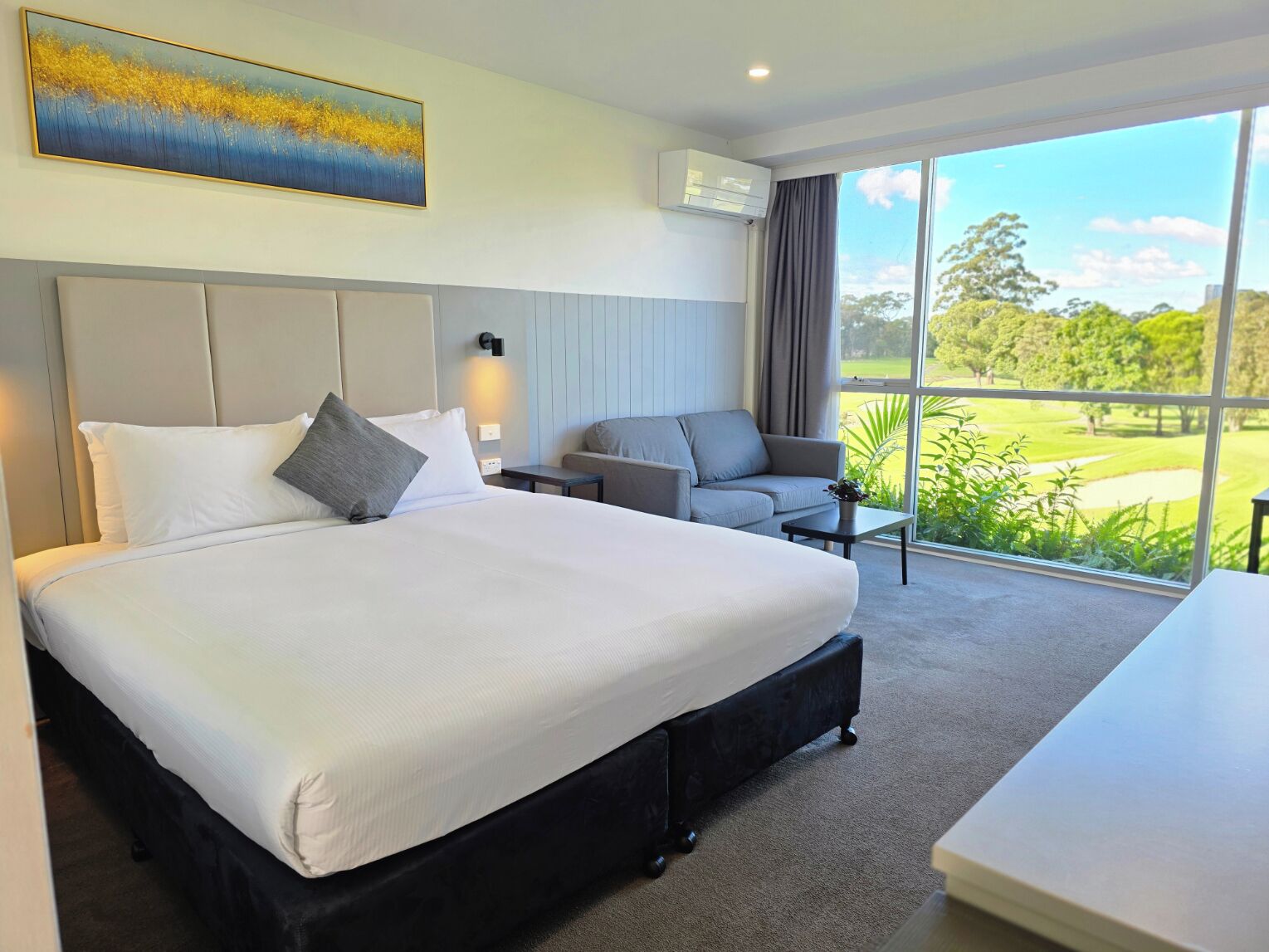 A hotel room with a large bed, a sofa, a small table, and a view of a golf course.
