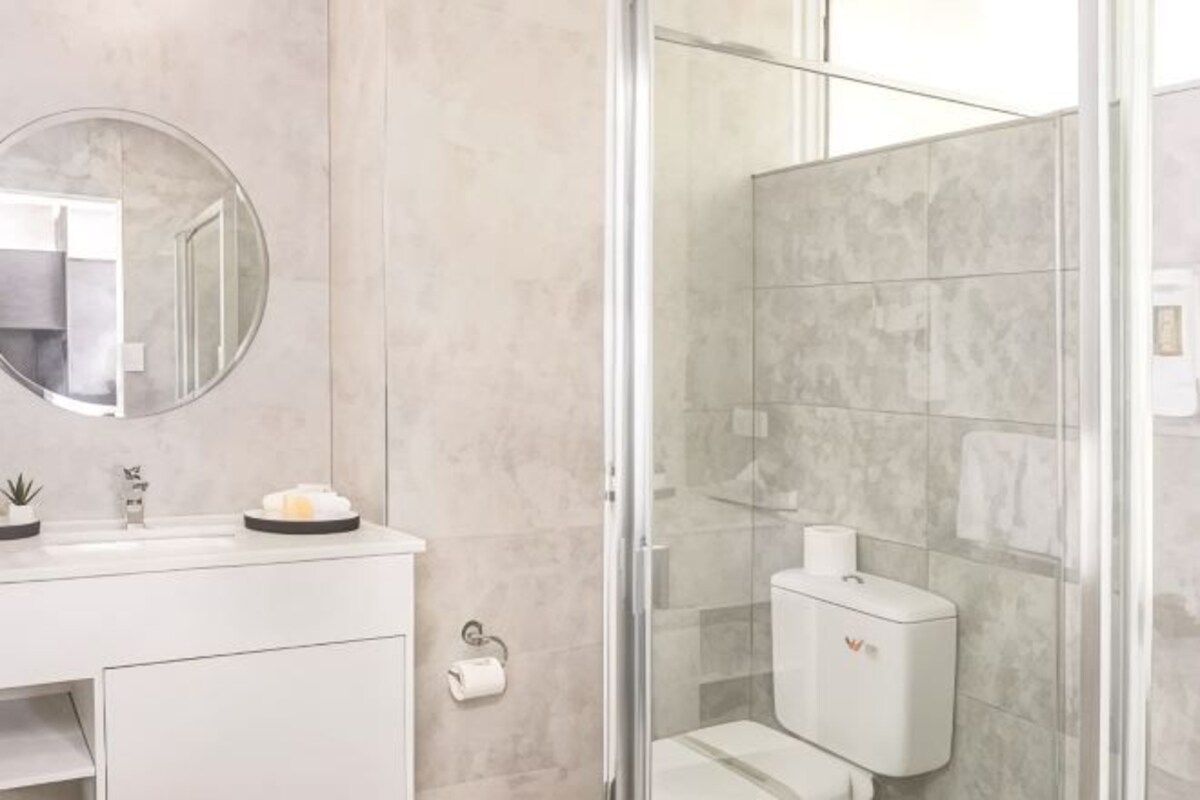 A bathroom with a toilet, a sink with a mirror, and a glass shower enclosure.