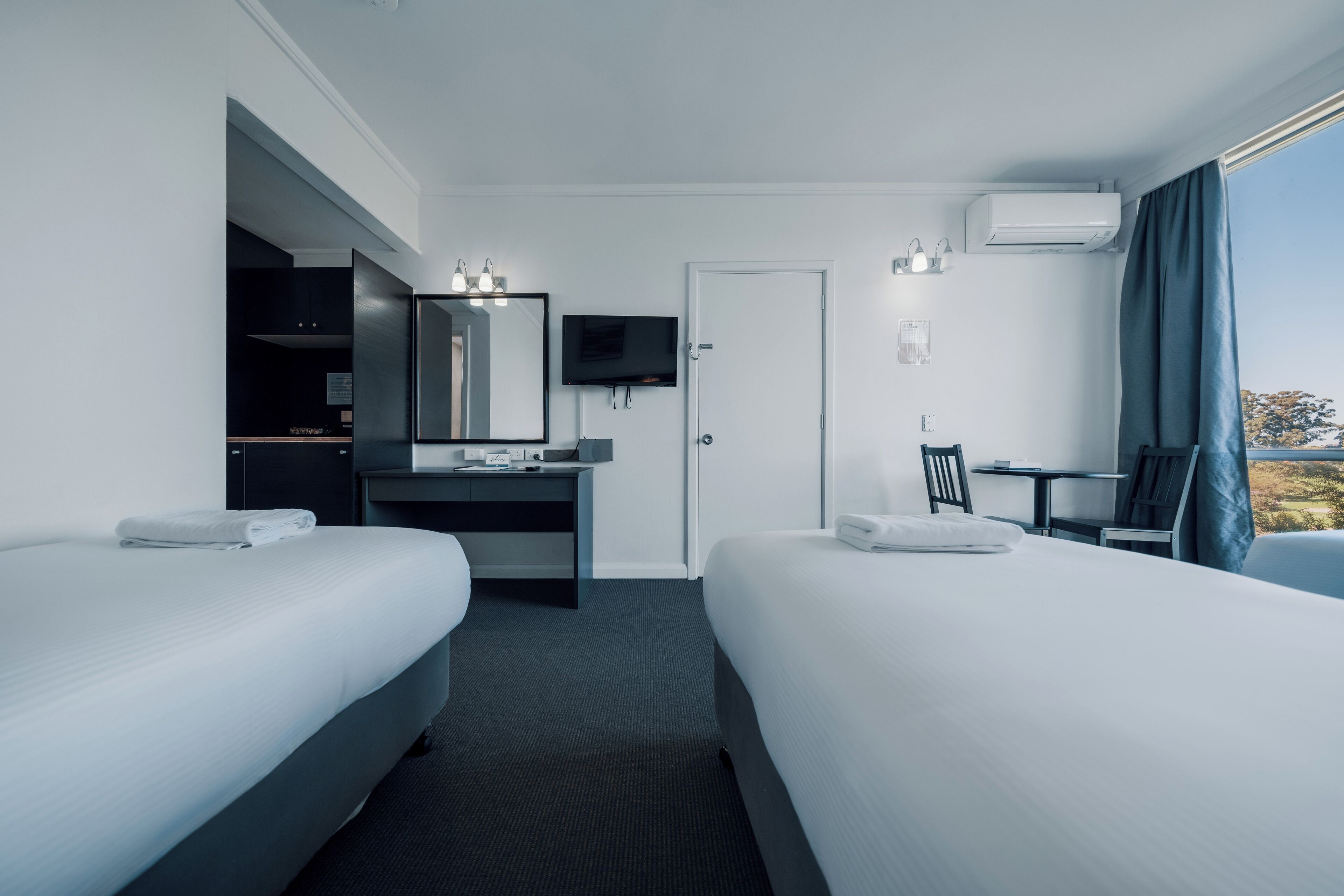 A hotel room with two beds, a desk with a mirror, a TV, and a window with curtains.