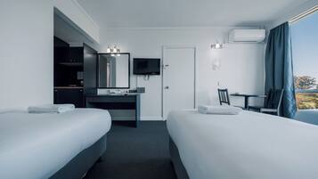 Una habitación de hotel con dos camas, un escritorio con espejo, televisión y ventana con cortinas.