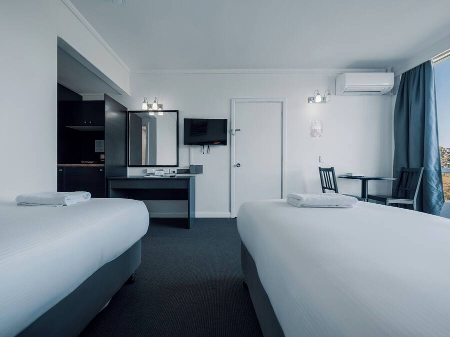 Una habitación de hotel con dos camas, un escritorio con espejo, televisión y ventana con cortinas.