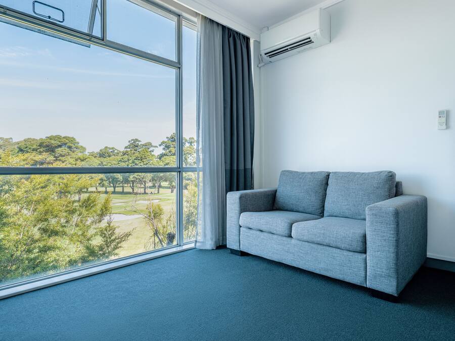 A room with a large window, a grey sofa, and a wooden panel on the wall.