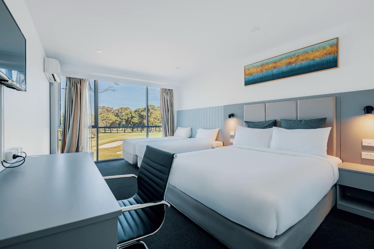 A hotel room with two beds, a desk, and a large window offering a view of a golf course.