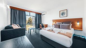 A modern hotel room with a large bed, a desk, a chair, and a view of the outdoors.