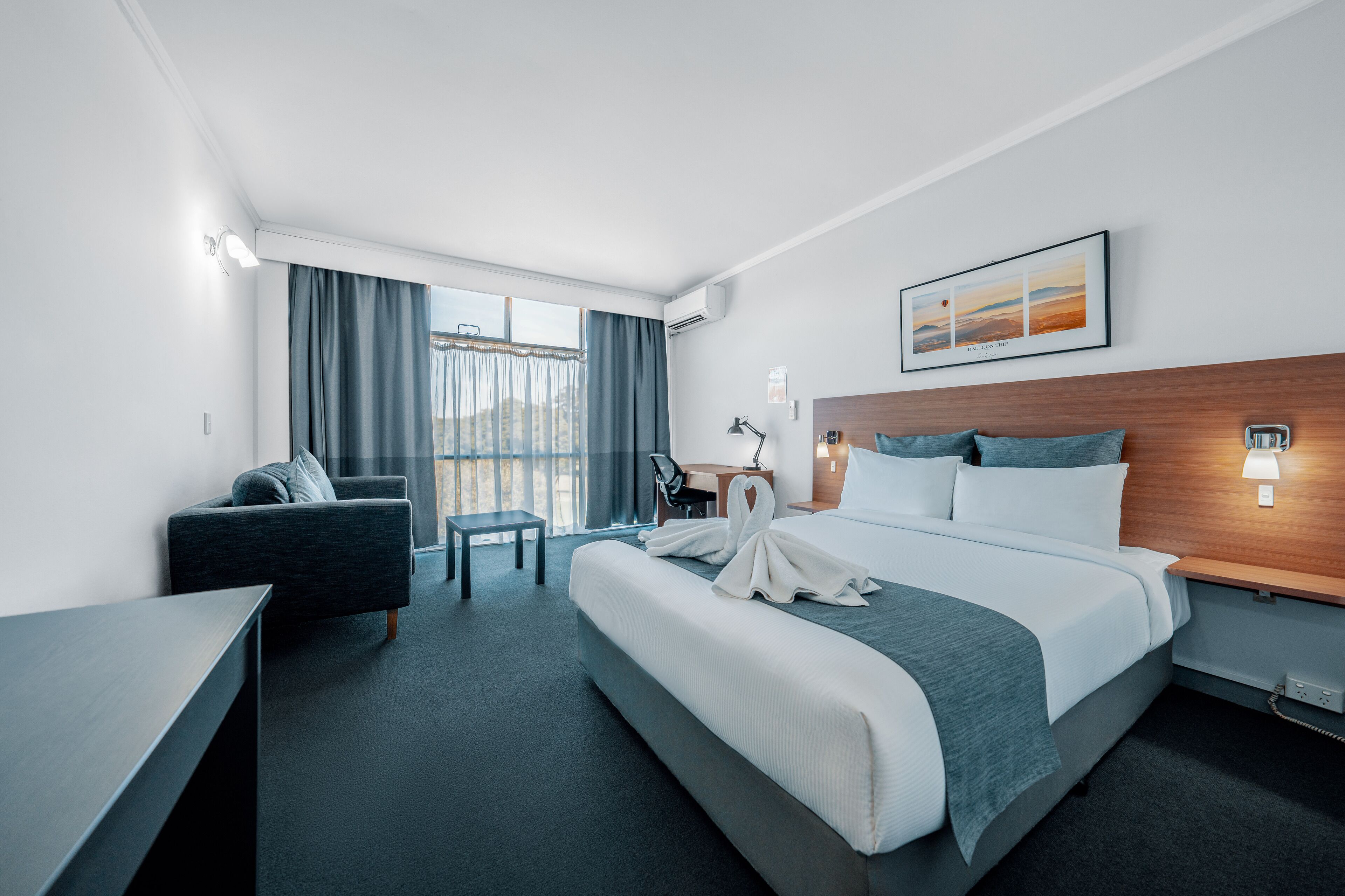Une chambre d’hôtel avec un grand lit, un bureau, une chaise, un canapé et une vue sur l’extérieur.